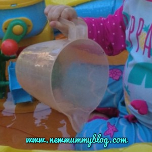 toddler using a plastic jug to pour water in a paddling pool