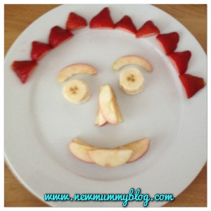 a face made from apple segments, bananas and strawberries